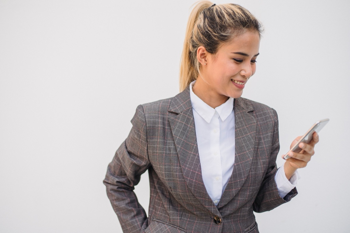 Mulher de terno sorrindo enquanto lê uma mensagem no celular