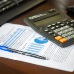 Calculadora e relatório financeiro sobre a mesa, representando a previsão de custo e lucro de um evento