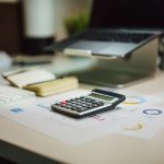 Calculadora sobre gráficos financeiros ao lado de laptop em mesa de escritório