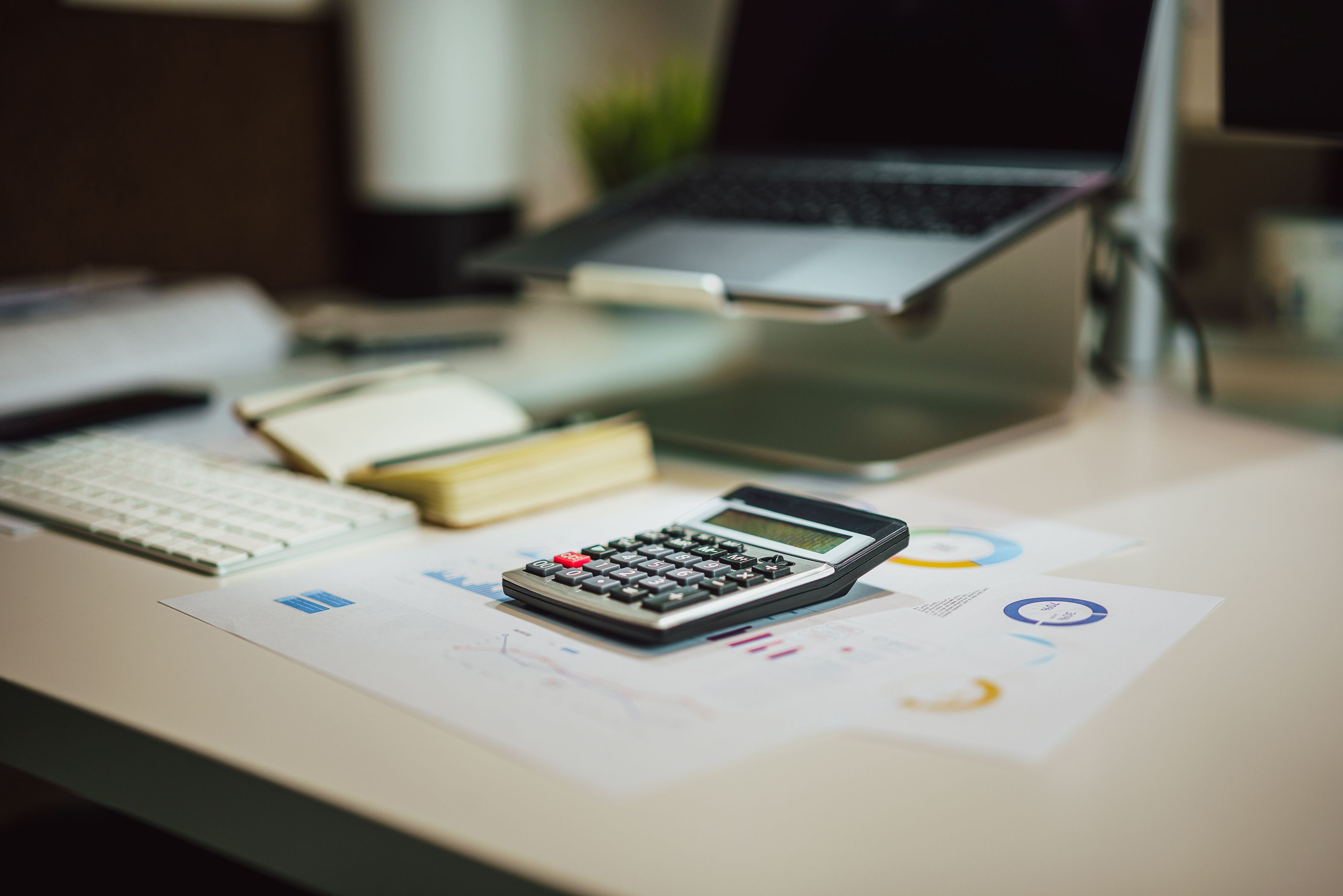 Calculadora sobre gráficos financeiros ao lado de laptop em mesa de escritório