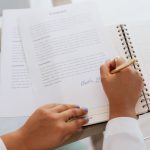 Pessoa assinando um contrato de prestação de serviço sobre uma mesa