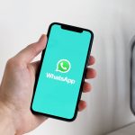 Mão segurando smartphone com a tela de abertura do WhatsApp