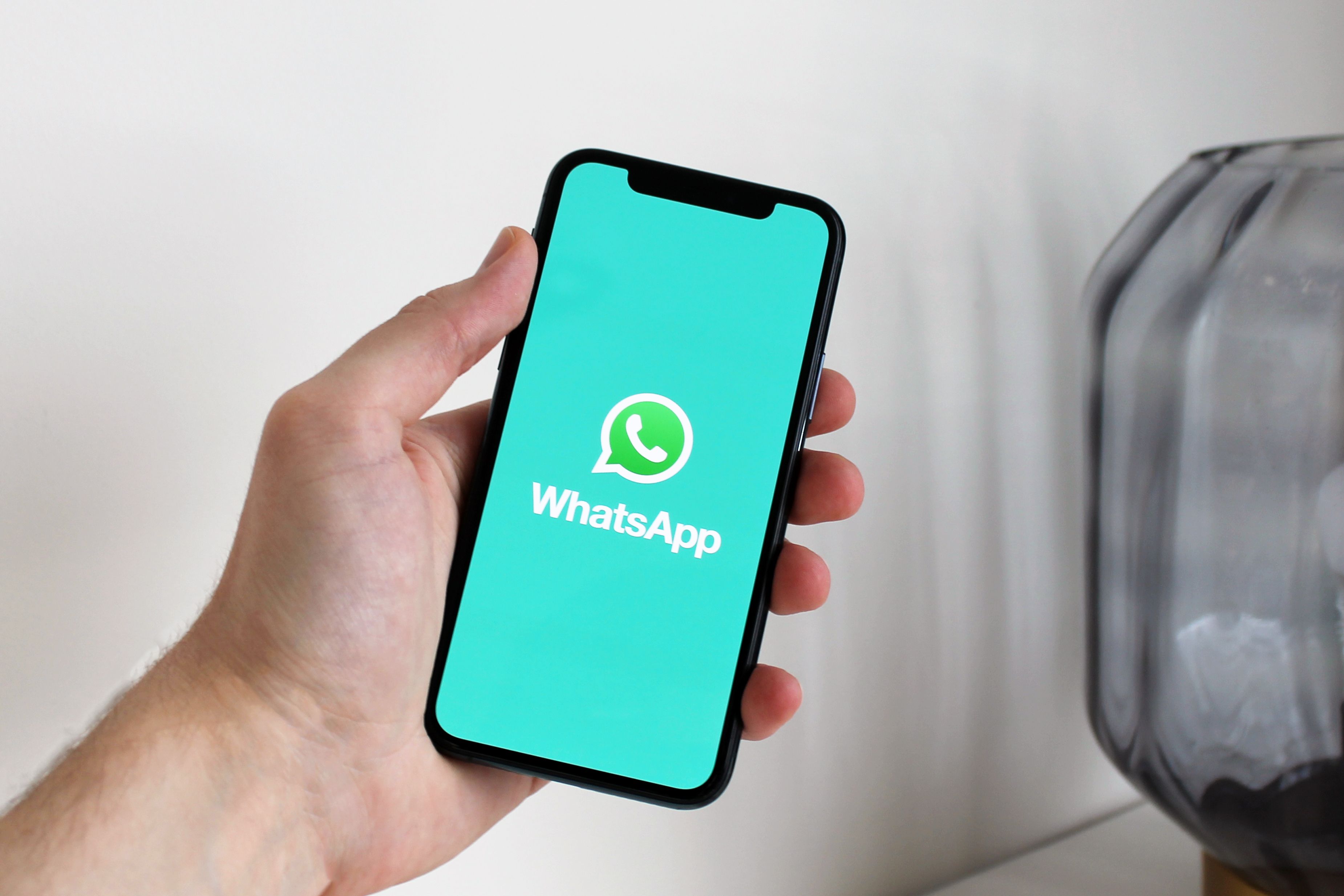 Mão segurando smartphone com a tela de abertura do WhatsApp