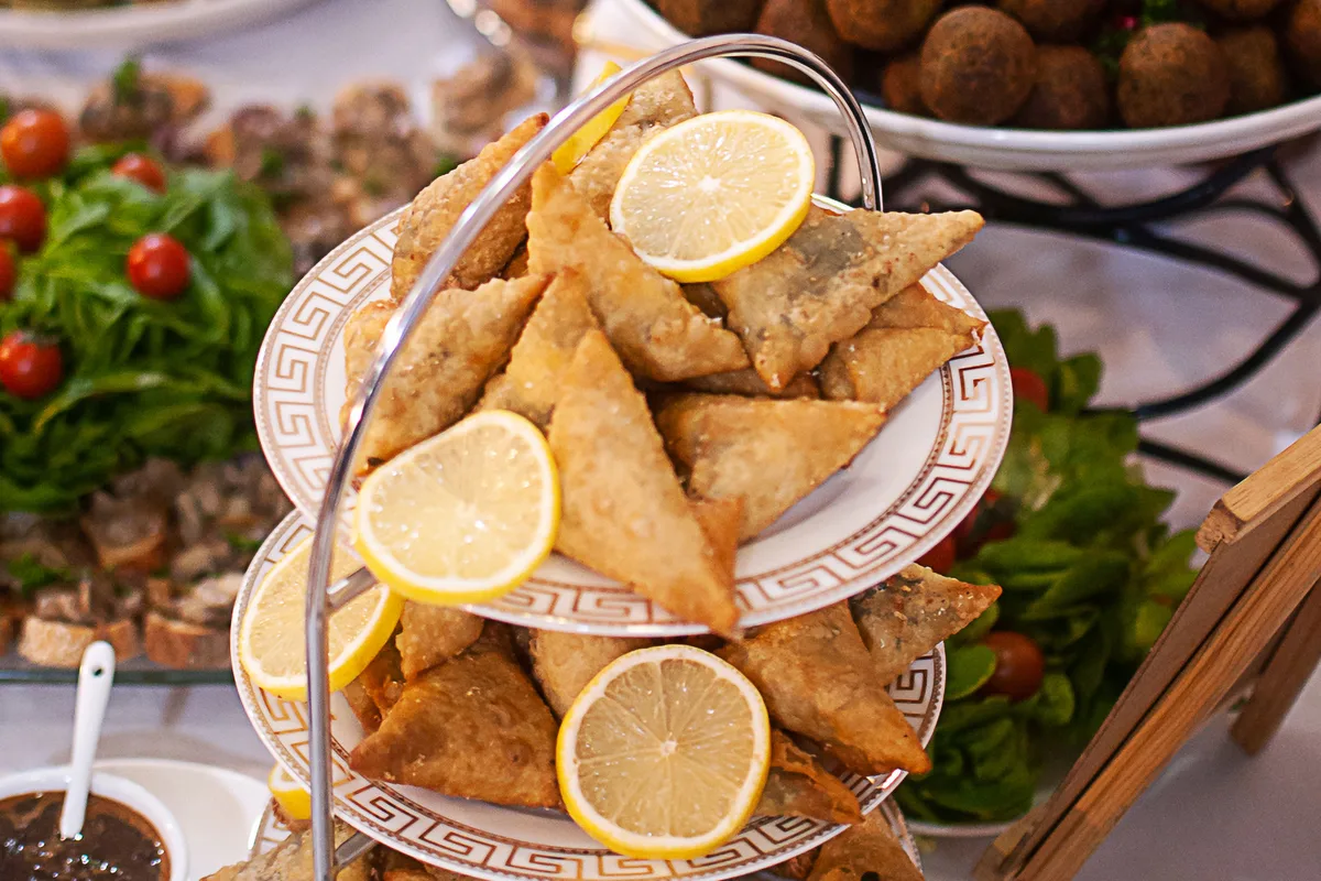 Bandejas de buffet com salgados, samosas e almôndegas decoradas com rodelas de limão