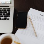Contrato, celular e notebook sobre a mesa, representando a assinatura eletrônica de contrato pelo WhatsApp